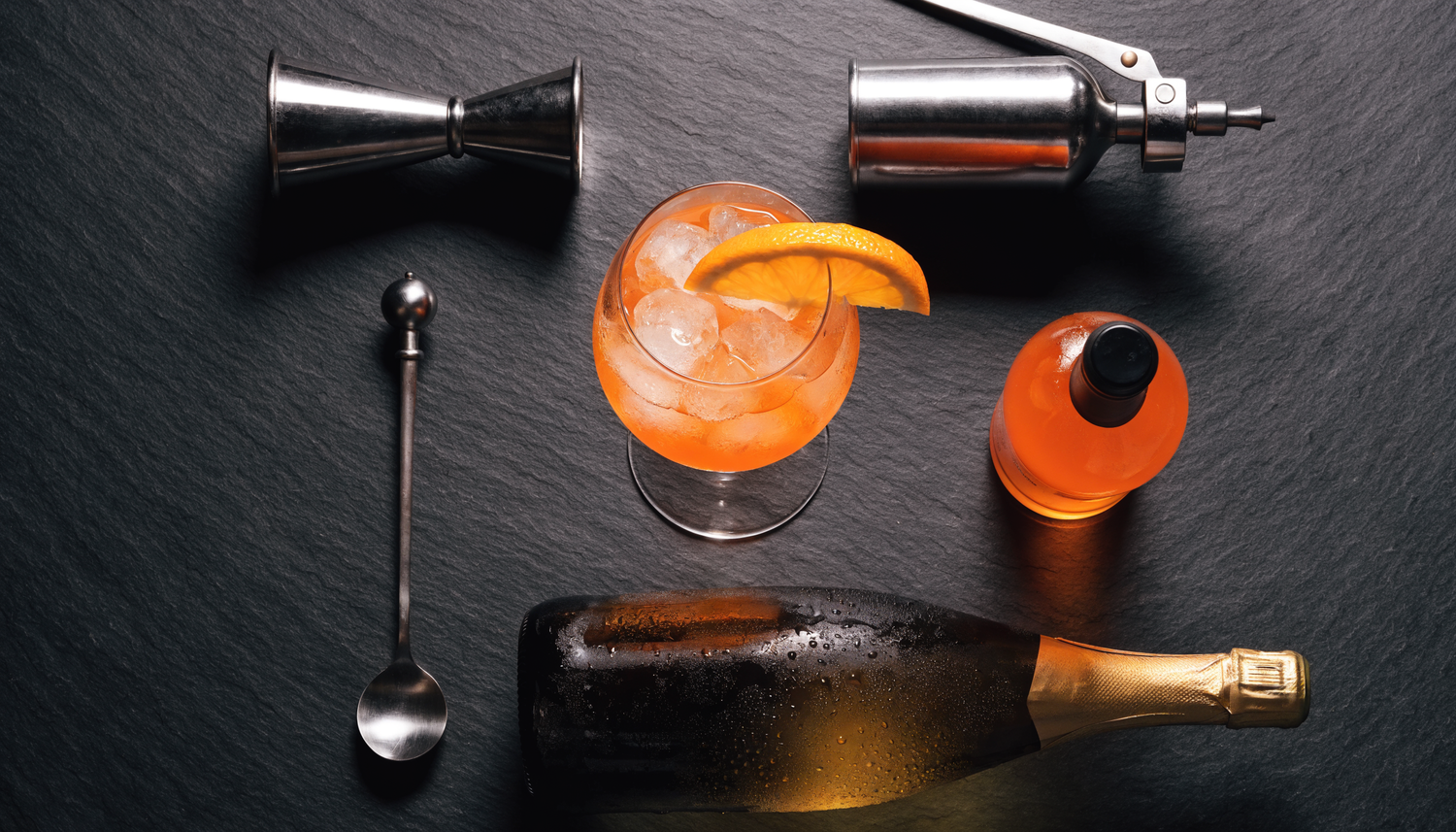 Jigger, barlepel en flessen rond een spritzglas, van bovenaf gefotografeerd